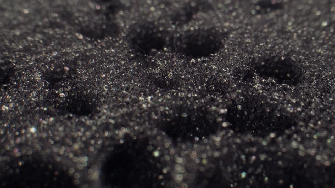 Macro Close-up of Shimmering Water Droplets on Black Foam
