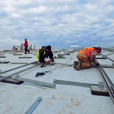 workers on the roof of flat building. engineers installing metal basis for future solar panels. construction of solar farm for renewable energy.