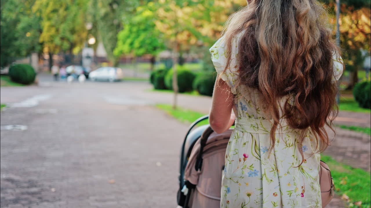 A woman in a floral dress pushing a baby stroller along a park path