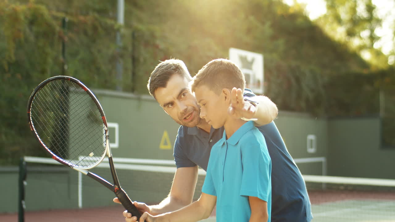 Man Teaching His Teen Son How To Play Tennis On A Summer Day 2
