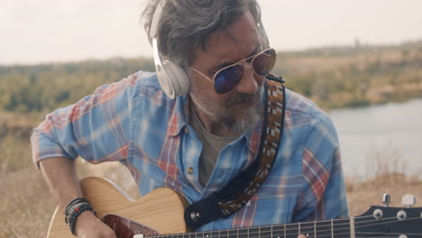 man playing acoustic guitar outdoors by a lake