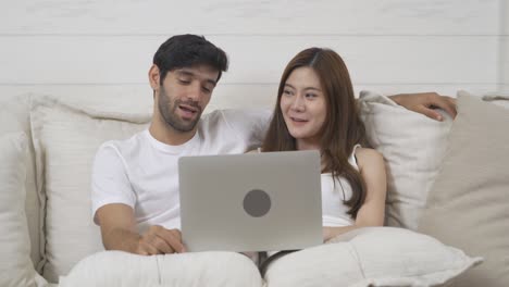 una pareja de familia. un joven feliz de oriente medio y una mujer asiática. personas que usan una computadora portátil en las redes sociales e internet y se sientan en safa en casa. estilo de vida en el dispositivo tecnológico.