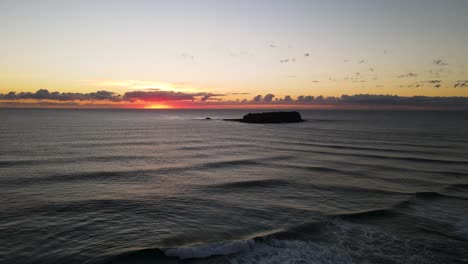 vista de drones en movimiento viajando sobre olas rompientes con una silueta de una isla de parque marino y un colorido amanecer en la distancia