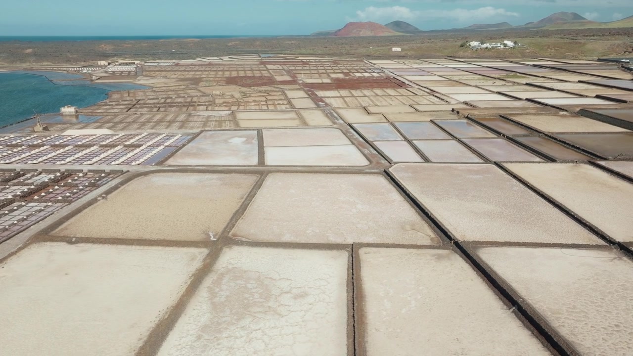 Vista aérea de drone das salinas de Janubio em Lanzarote, Espanha, com tanques de sal geométricos, litoral e montanhas vulcânicas ao fundo. Parte 3.