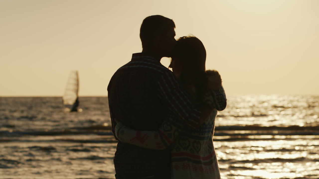 silueta de una pareja amorosa abrazándose al atardecer cerca del velero del mar flota en la distancia