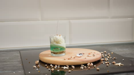 chandler carefully places candle mold on wooden tray surrounded by scattered shell decorations and beads on table surface while organizing workspace in preparation for product display or packaging