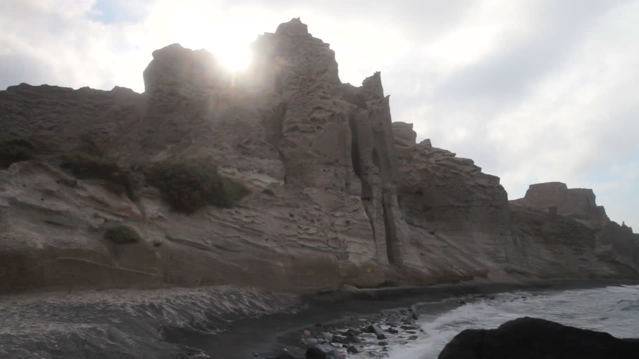 toma de seguimiento de olas golpeando una playa negra rodeada de formaciones de acantilados volcánicos blancos en santorini, grecia