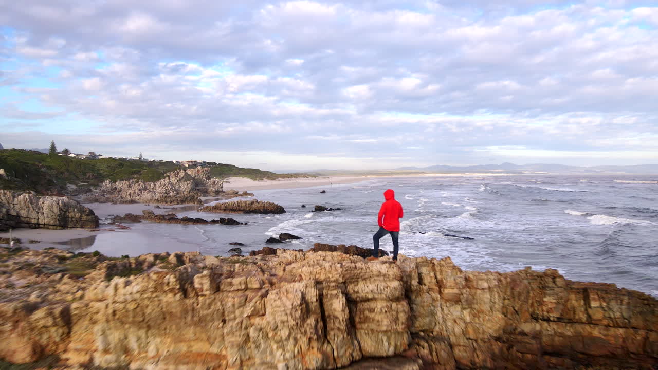 Man on jagged coastal rocks look out over Grotto Blue Flag beach