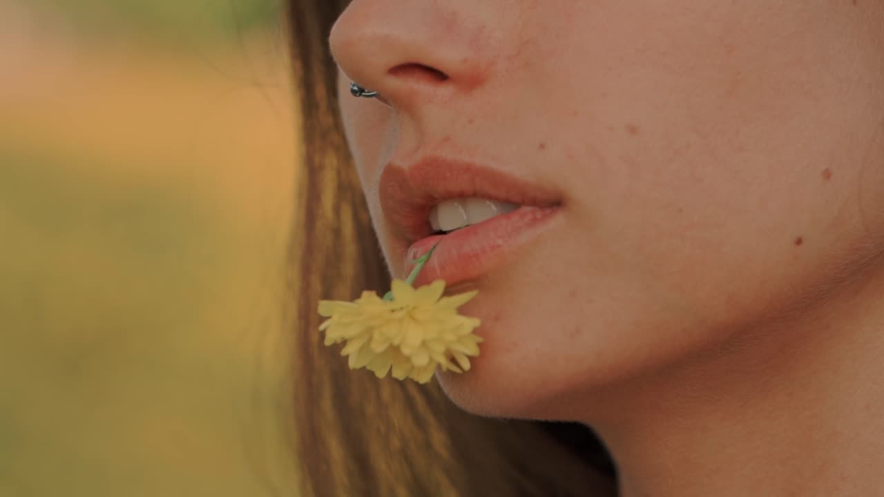 Primo piano di una giovane donna che tiene un fiore giallo in bocca.