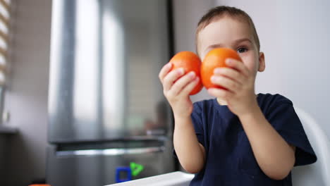 Lovely baby is eating and playing with tangerines. Cute child puts the fruit covering his eyes. Close up.