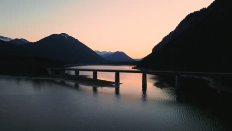 sunset aerial drone flight above the scenic and idyllic sylvensteinspeicher fresh drinking water sylvenstein reservoir bridge in the bavarian austrian alps with mountains and clear blue water below