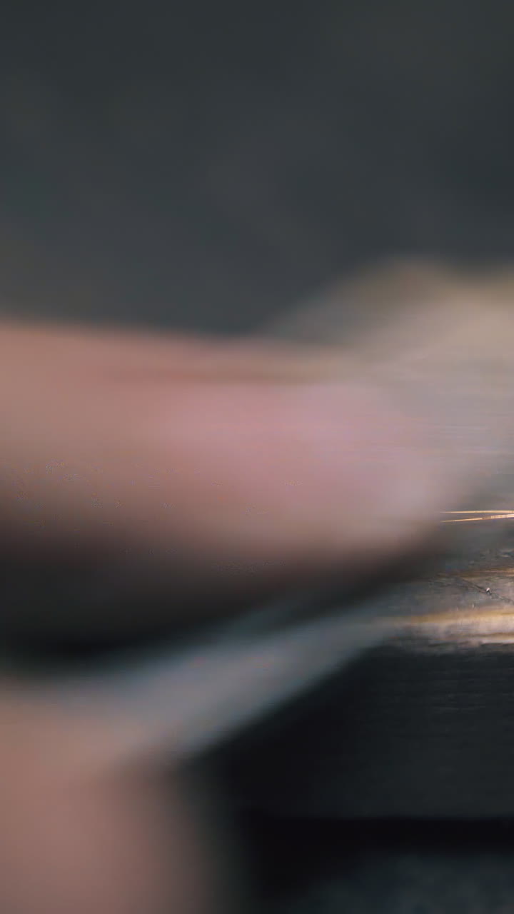 CU: skilled goldsmith grinds elegant shining bracelet with rasp on wooden gutter at dark table in workshop close view