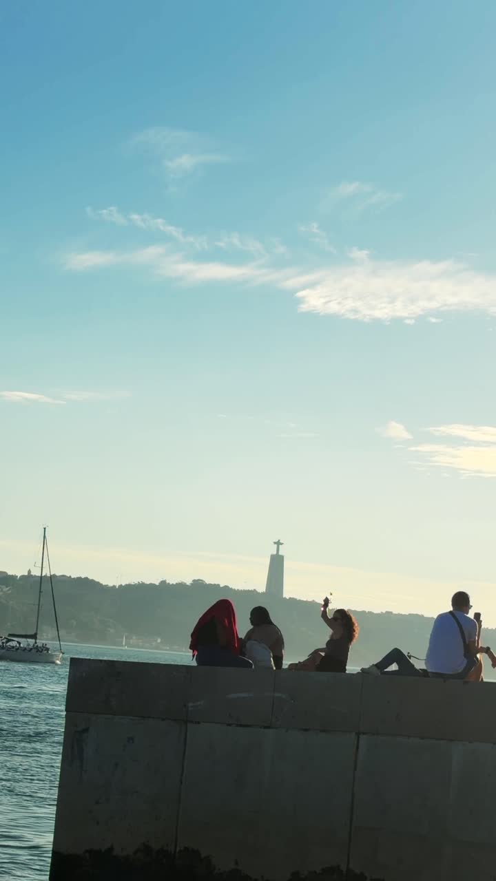 People enjoying the sunset by the ocean with Christ the King statue in the background
