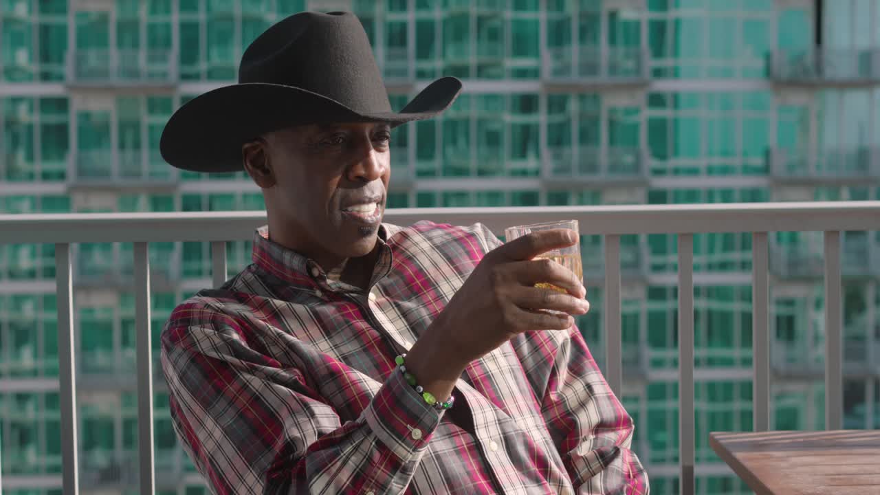 disparo panorámico de un hombre negro con sombrero de vaquero sosteniendo una taza de vidrio