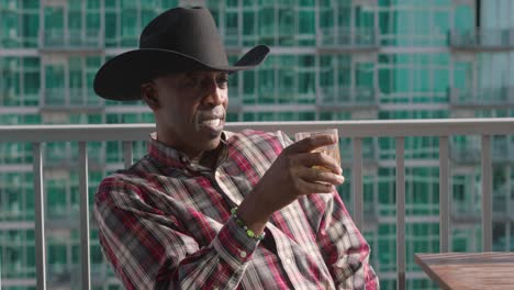 disparo panorámico de un hombre negro con sombrero de vaquero sosteniendo una taza de vidrio