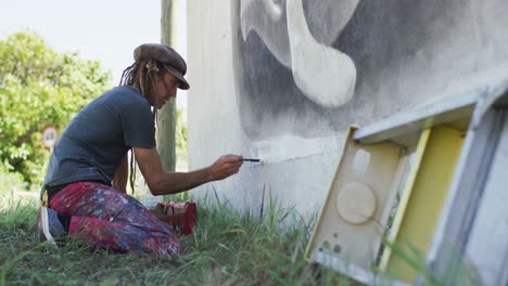 video of caucasian male artist with dreadlocks kneeling painting whale mural on wall