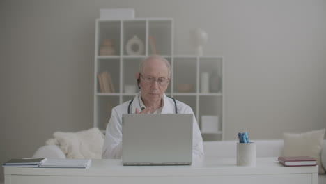 aged male physician is working remotely from his office in clinic using laptop for communication with colleagues