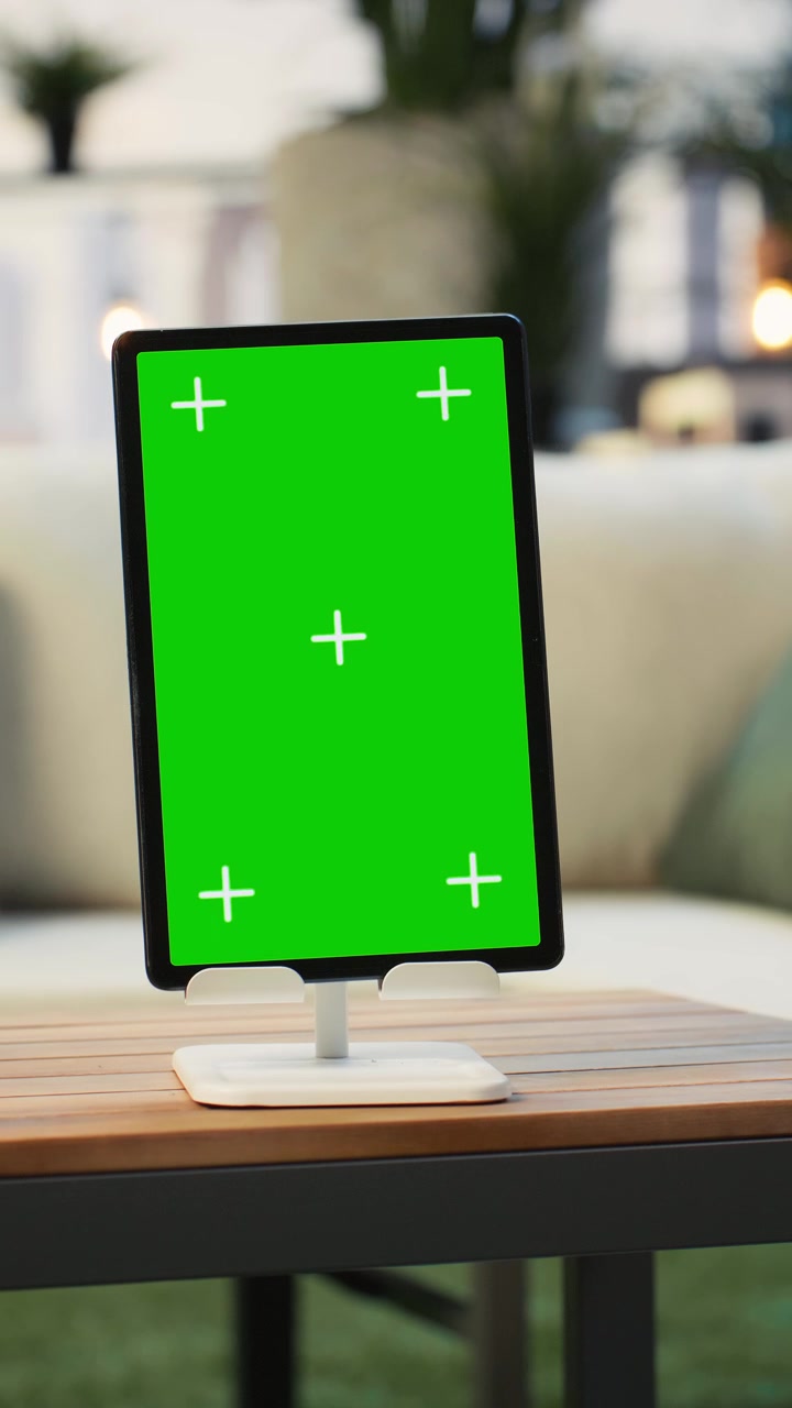 Video verticale: tablet con schermo verde su tavolo di legno con piante sullo sfondo, ripresa panoramica
