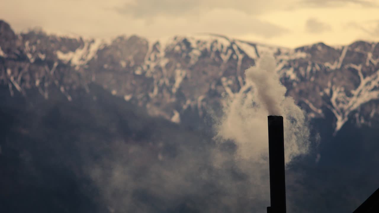 루마니아 시골에서 봄의 황혼이 지나는 동안 배경에 부체기 산맥이 있는 금속 굴에서 연기가 아오르고 있다.