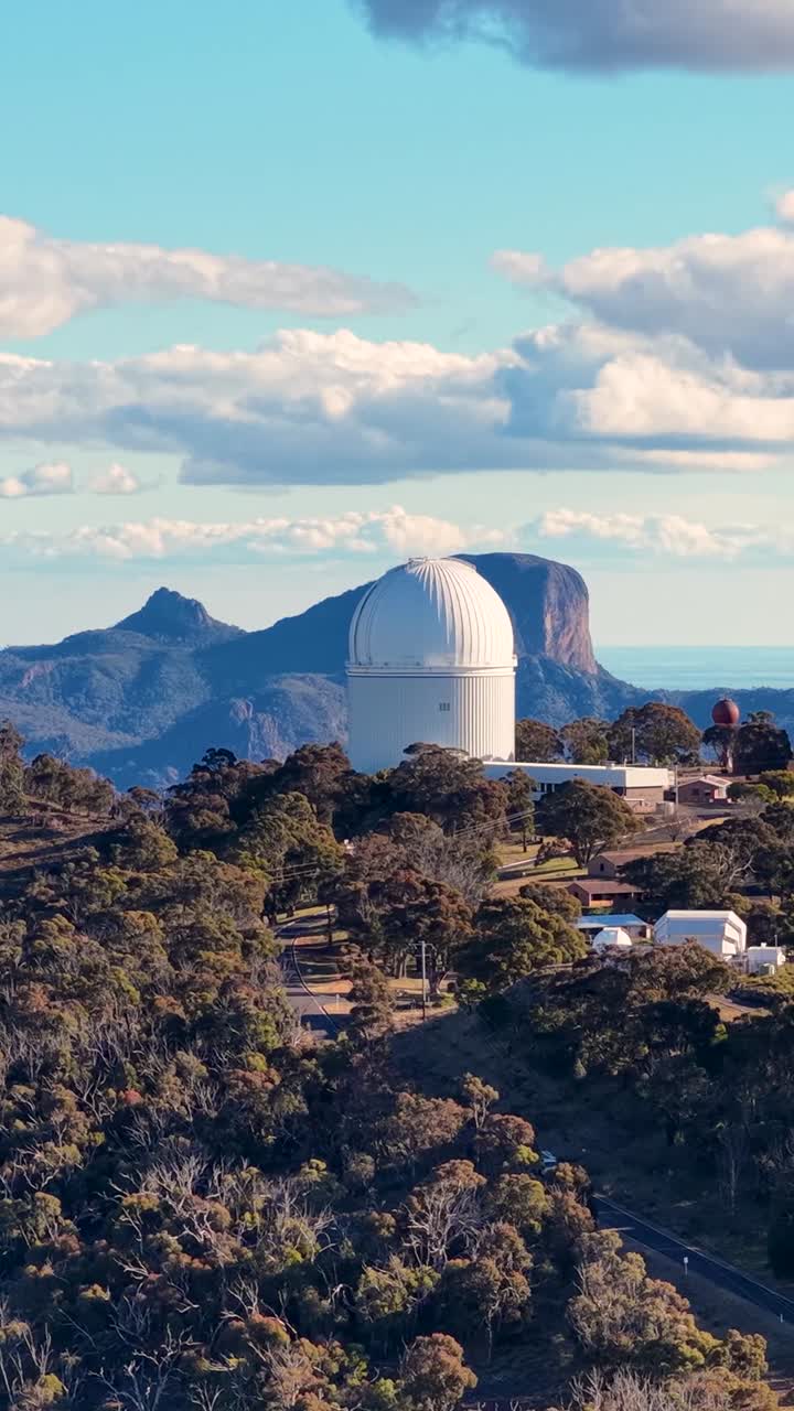 Drone footage captures a large astronomical observatory dome nestled within a rugged, forested mountain landscape