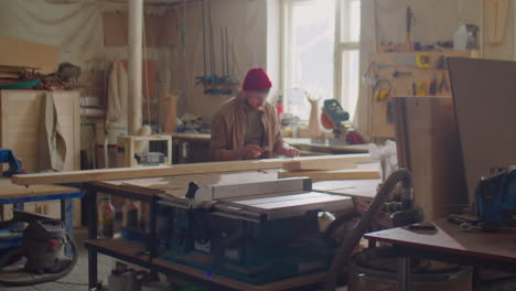 carpenter taking measurements of wooden plank in workshop
