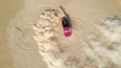 Red-truck-drifting-doughnuts-in-the-dusty-desert-sand,-aerial-top-view