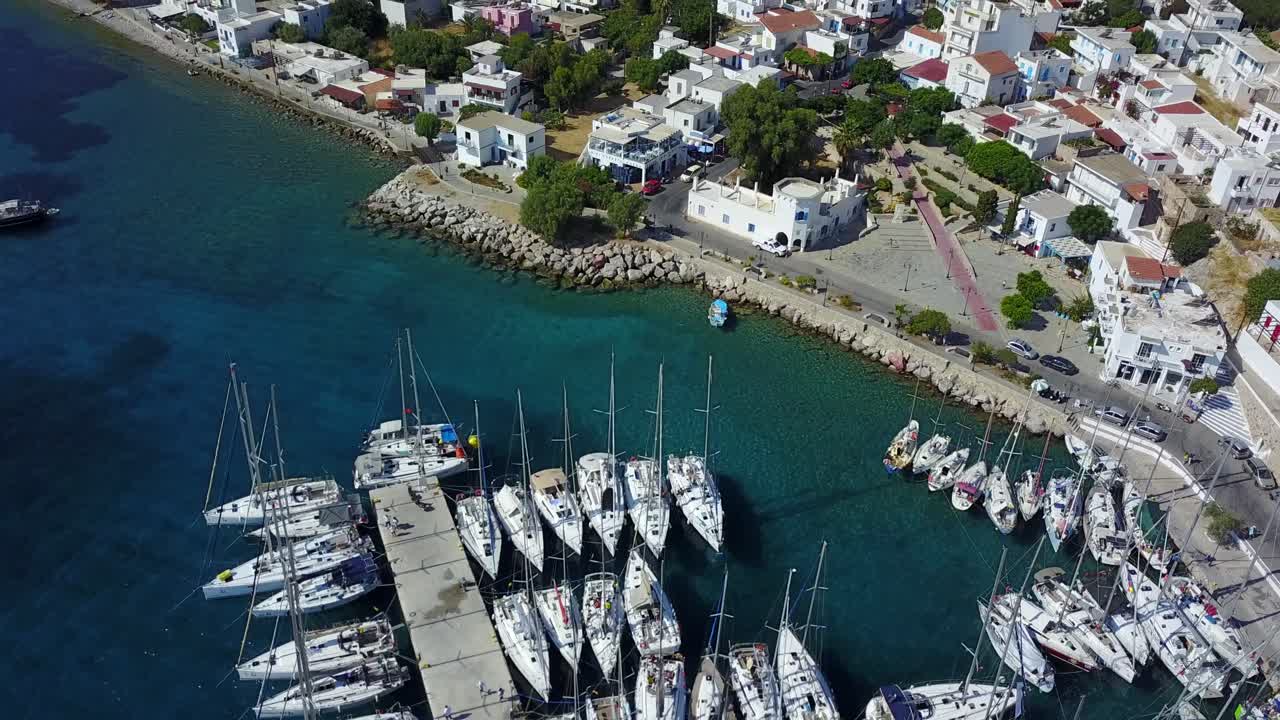 Drone rising shot over small harbour on Tilos island in Greece with opening panorama of a small greek style town