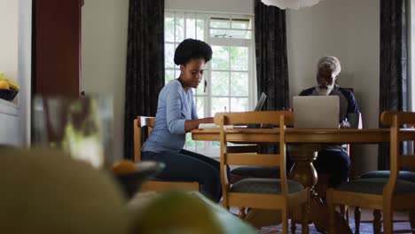african american couple sitting at dining table using laptops paying bills