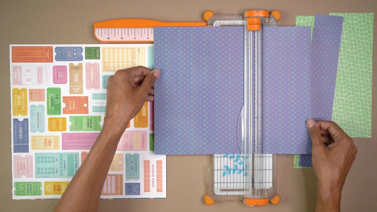 Hands trim blue patterned scrapbook paper with a tabletop cutter for handmade craft