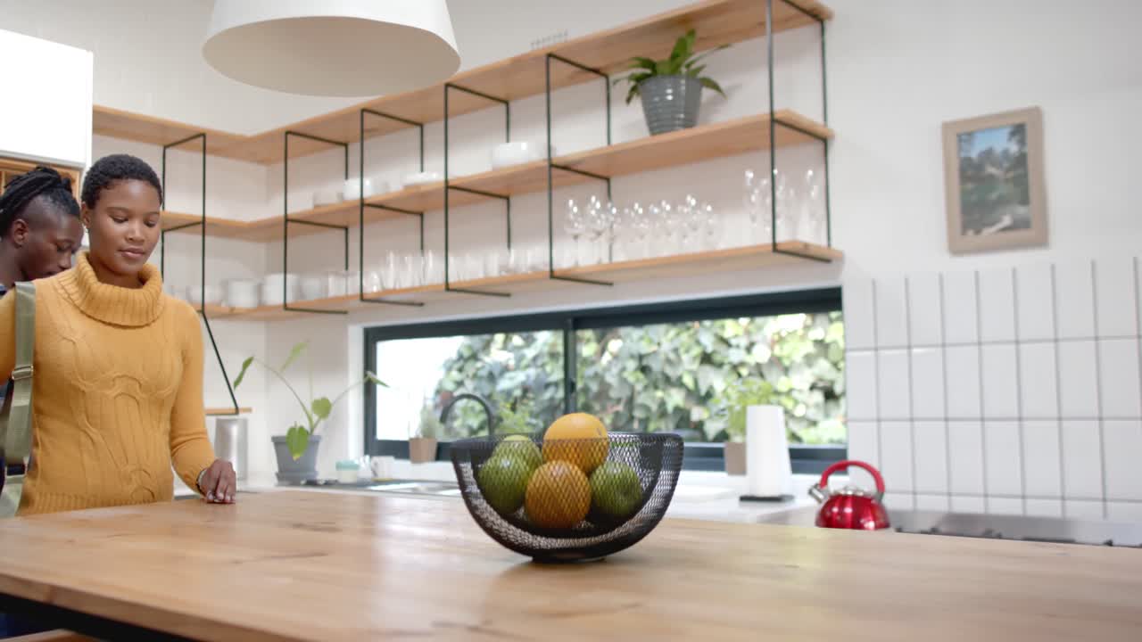 feliz pareja afroamericana desempaquetando comestibles en la cocina, cámara lenta