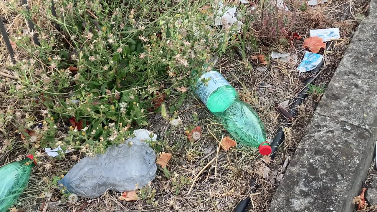 Primo piano statico di una bottiglia di plastica abbandonata a terra. Simbolo dell'inquinamento urbano, dell'abbandono sconsiderato di rifiuti e dell'impatto ambientale dell'uso problematico della plastica.