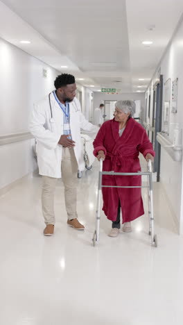 vertical video of diverse male doctor talking and walking with senior female patient in slow motion