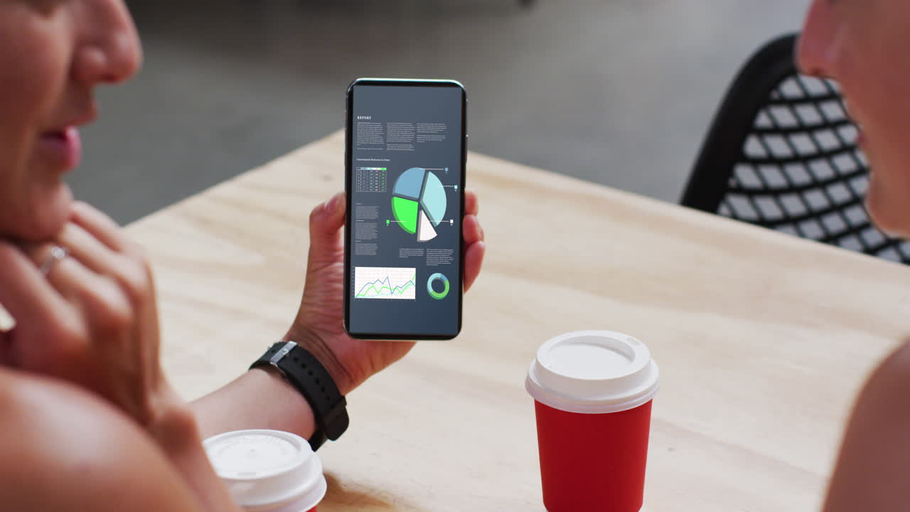 hombre y mujer caucásicos sentados a la mesa, usando un teléfono inteligente con estadísticas en la pantalla