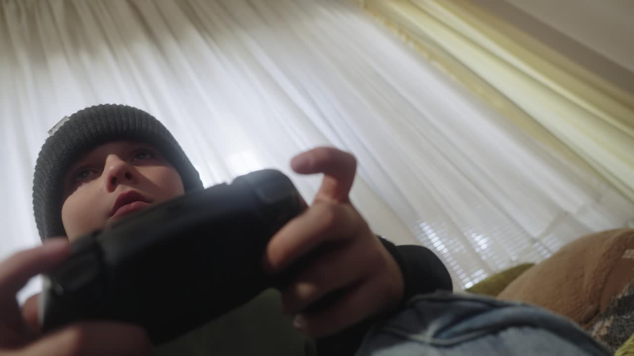 소파에 앉아 플레이스테이션 컨트롤러로 게임을 하는 어린 소년의 극적인 낮은 각도 시각