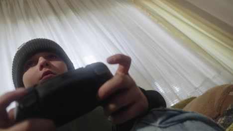 a dramatic low-angle view of a young boy sitting on a couch playing a game with a playstation controller