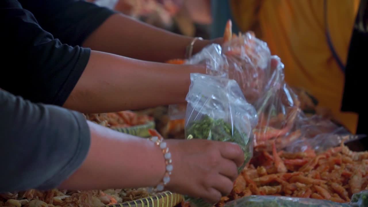 The seller's hand puts the seafood product on the plastic bag for customer