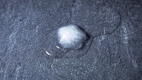 lapso de tiempo de fusión del cubo de hielo blanco de congelado a líquido en primer plano sobre una piedra gris