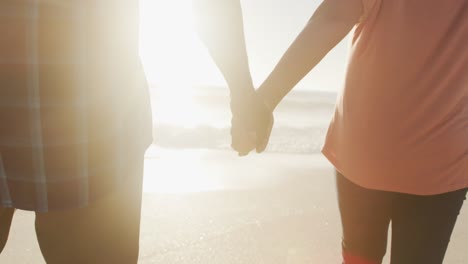 senior african american couple holding hands and walking on sunny beach