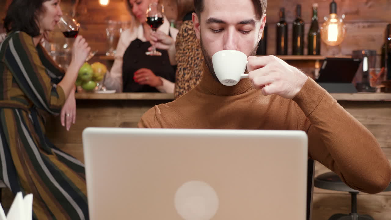 Man working on laptop in a bar with people in the background