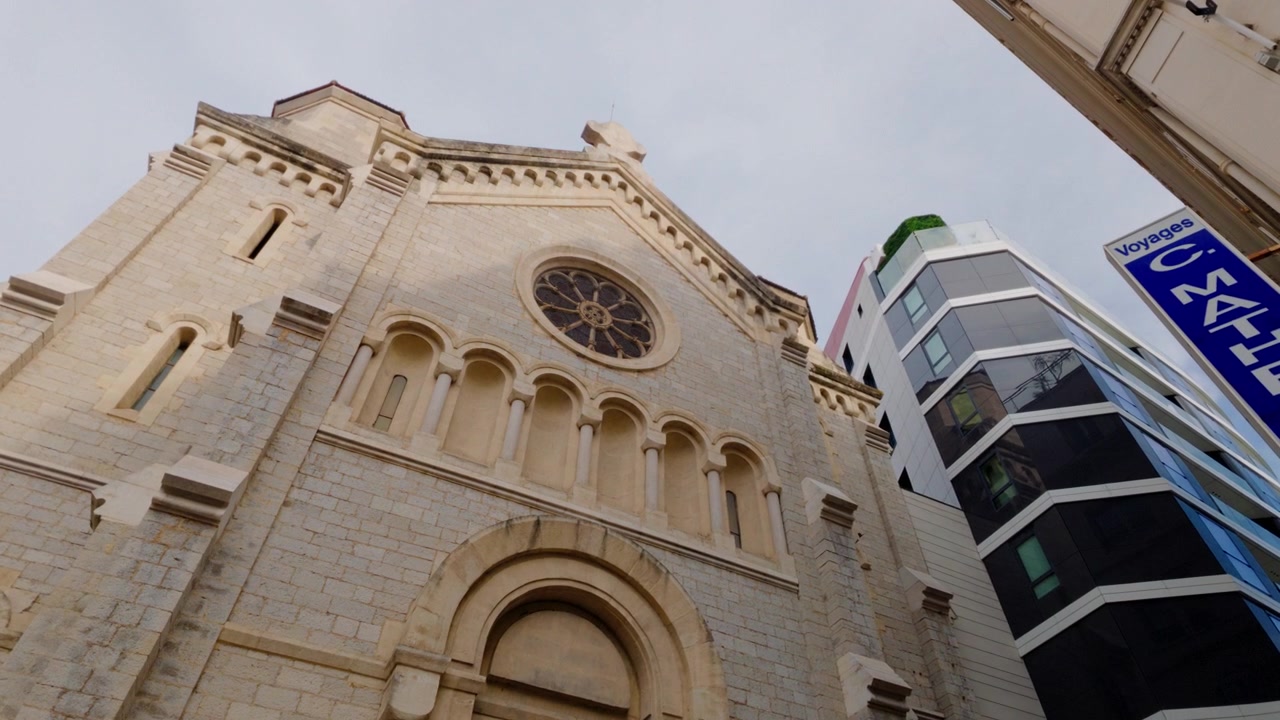 Facciata di una chiesa in pietra con rosone accanto a edifici moderni nel centro della città di Cannes