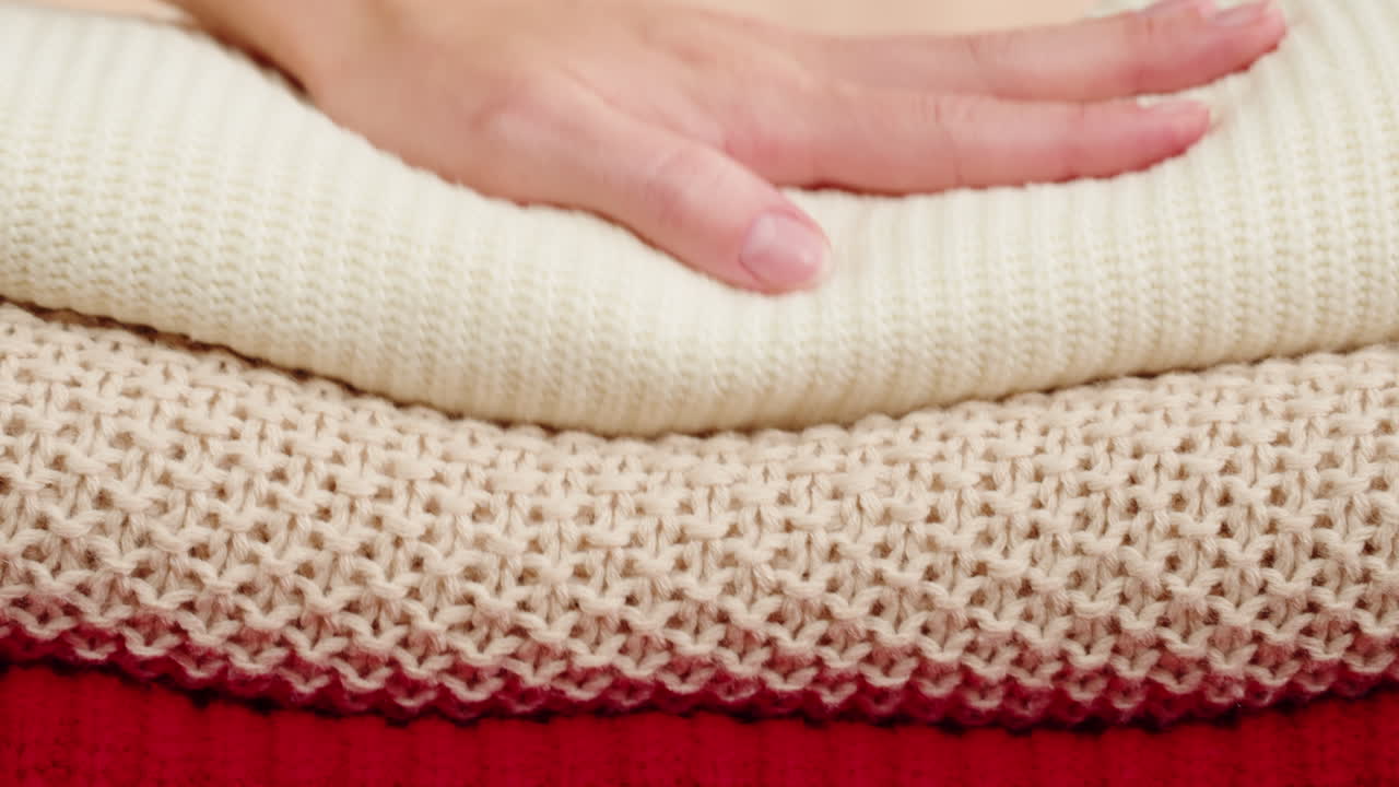 Woman's hand arranging stacked knitted sweaters