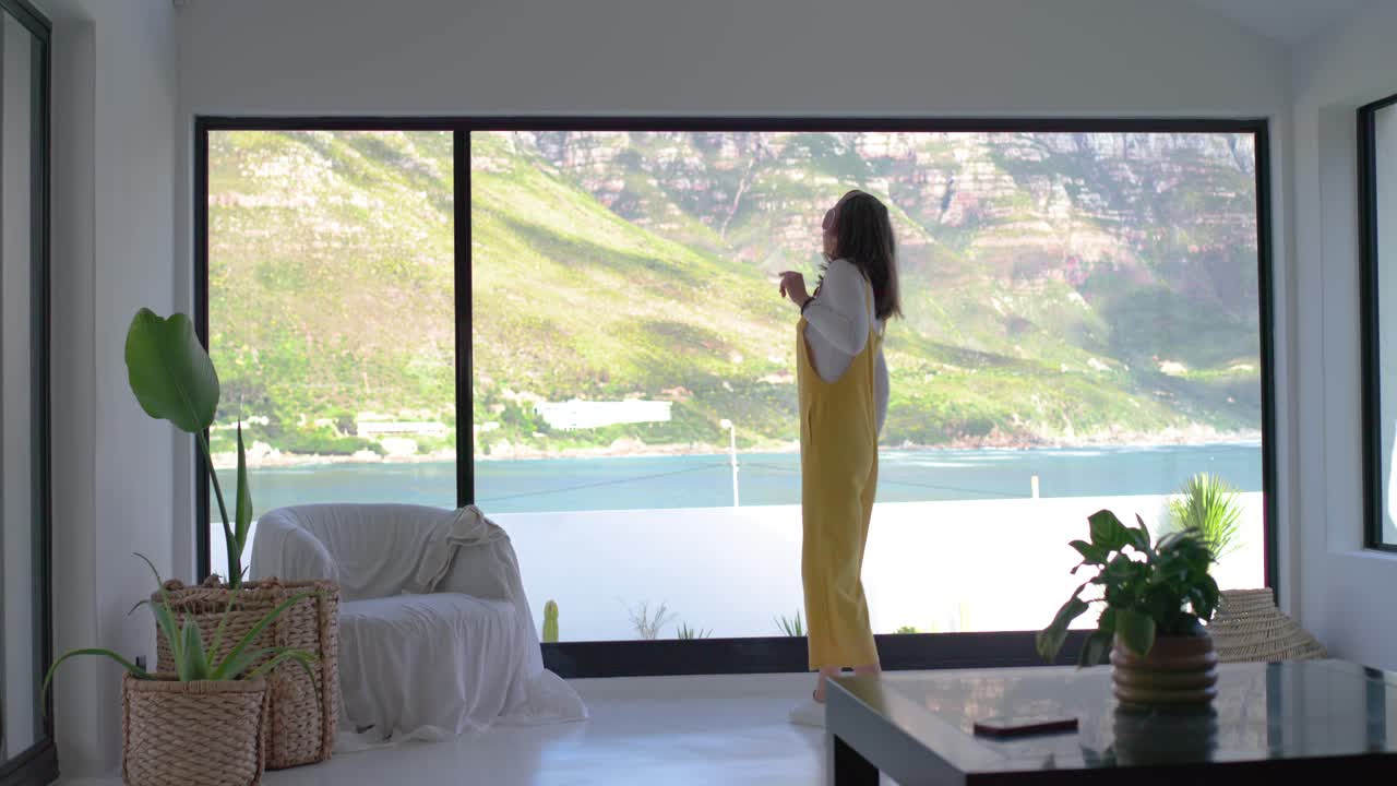 Mujer entrando por la derecha, cogiendo el teléfono y los auriculares mientras escucha música y baila junto a la ventana.