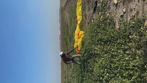 vertical format: paraglider pilot arranges yellow canopy on ground