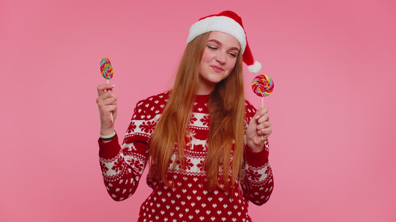 Joyful girl in christmas sweater hat holding candy striped lollipops dancing making silly faces