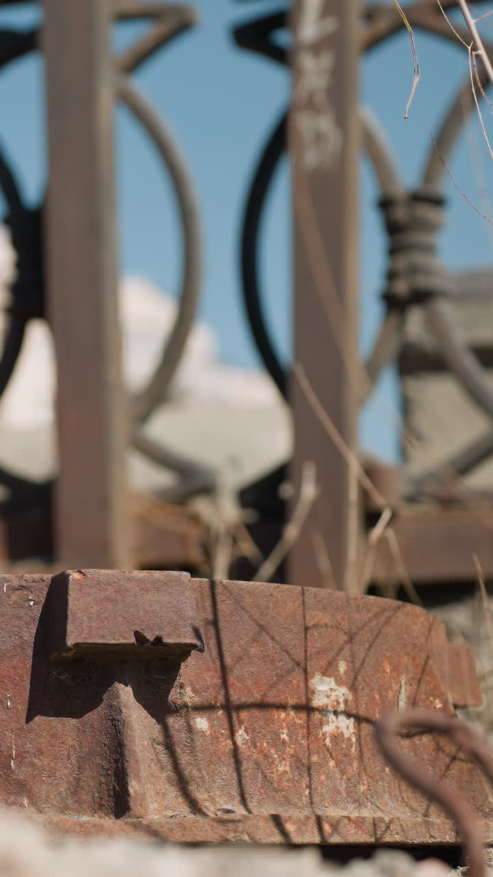 vista cercana de un objeto metálico oxidado tendido en el suelo con una valla urbana adornada y un coche blanco borroso en movimiento con otros coches