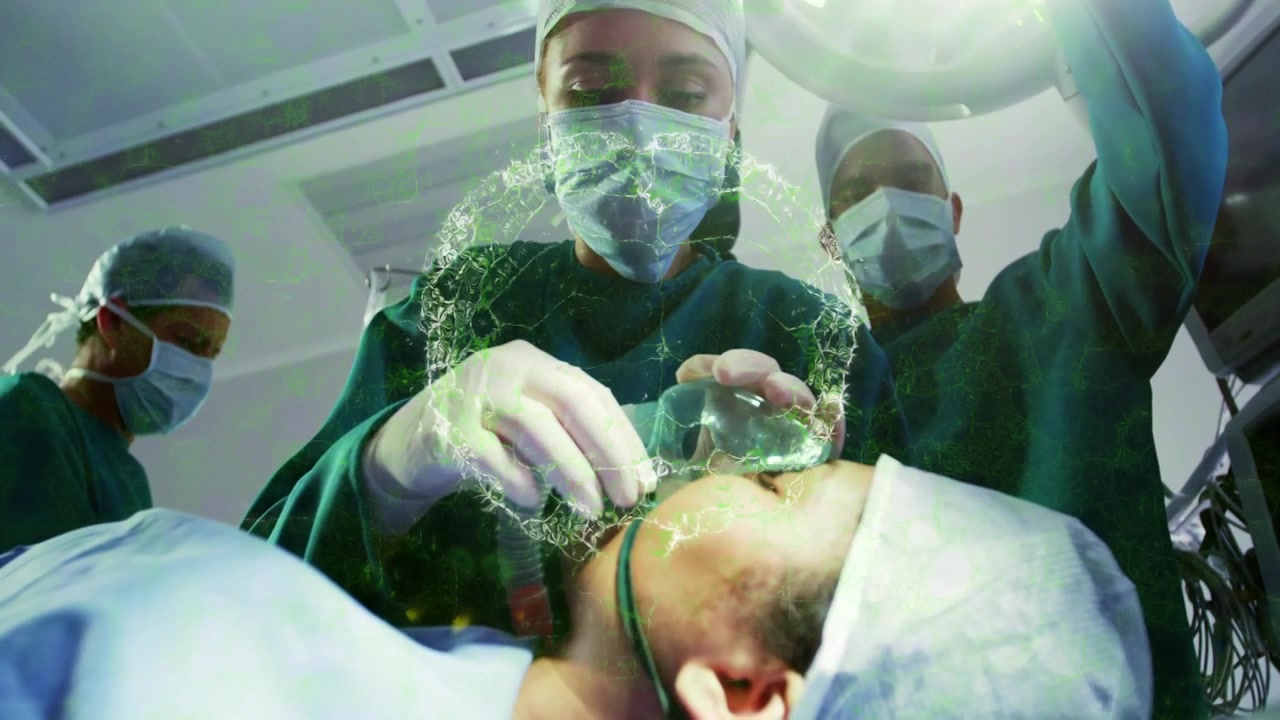 Kirurg fäster mask, startar grön hologram för synlighet medan teamet höjer ljuset och kontrollerar dropp.