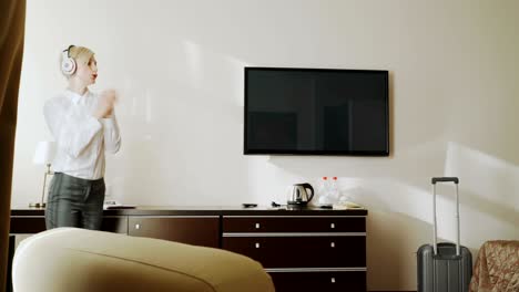 happy businesswoman dancing and singing while listening music on wireless headphones while have fun walking at hotel room. travel, business and people concept