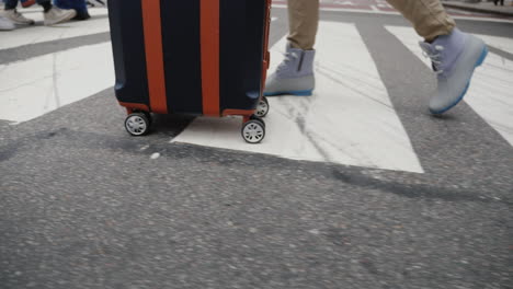 A-Woman-With-A-Travel-Bag-On-Wheels-Goes-To-A-Pedestrian-Crossing-In-A-Crowd-Of-People-Only-Legs-Are