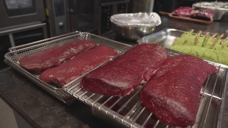 big venison meat slices on a metal tray on kitchen table, before baking in oven