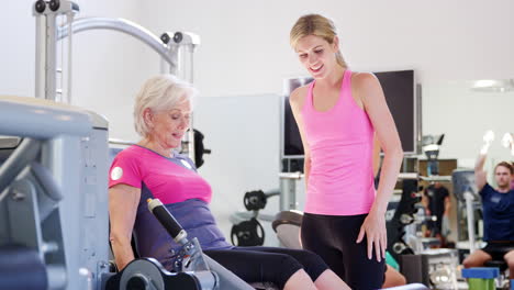 Mujer-Mayor-Haciendo-Ejercicio-En-Equipos-De-Gimnasio-Siendo-Alentada-Por-Un-Entrenador-Personal